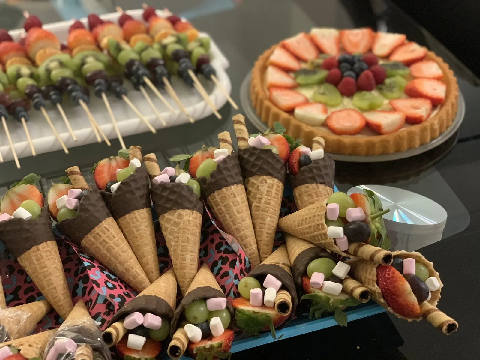 Espetinhos de frutas, uma torta de frutas e casquinhas recheadas de frutas